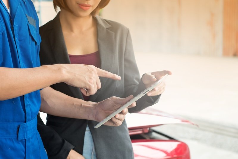 Machanic man shows report on tablet to woman customer at garage, A man mechanic and woman customer discussing repairs done to her vehicle.