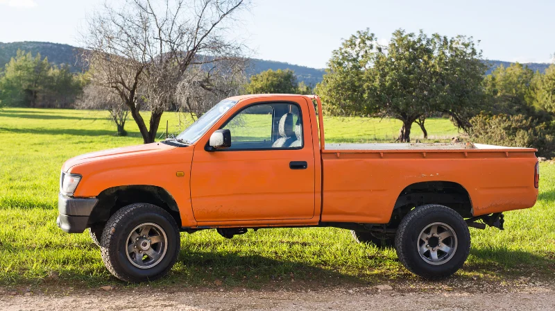orange pickup truck on grass roadside